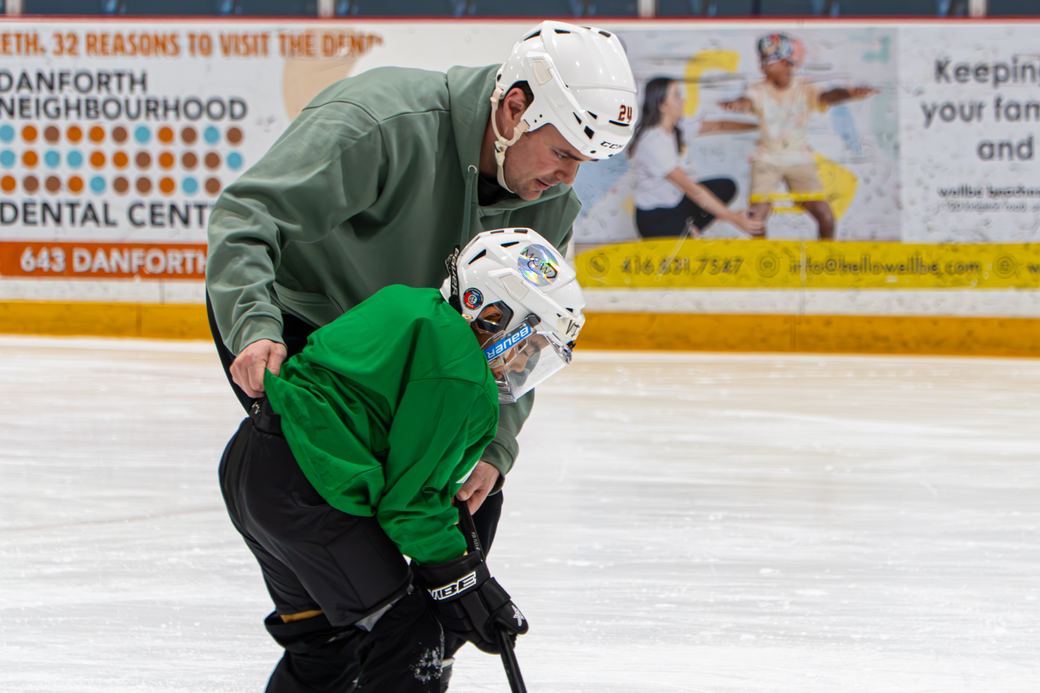 A coach bent low demonstrating a stride to a camper in green