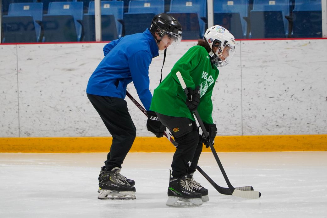A coach skating alongside a camper in green during a drill