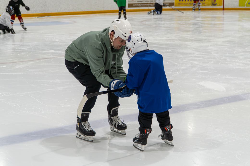 A coach in a green hoodie showing two campers how to hold their sticks