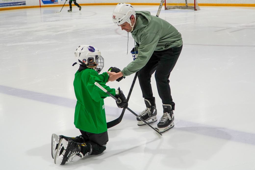 A volunteer kneeling to steady a camper who is finding their balance for the first time
