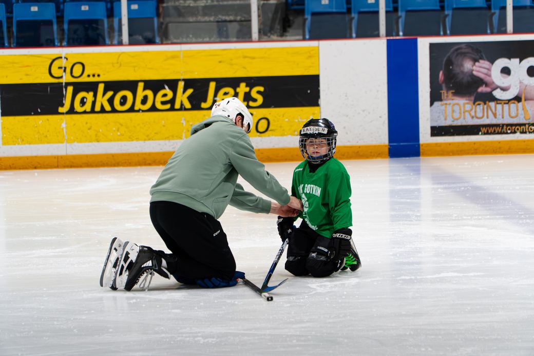 A volunteer crouched at ice level, eye to eye with a first-time skater