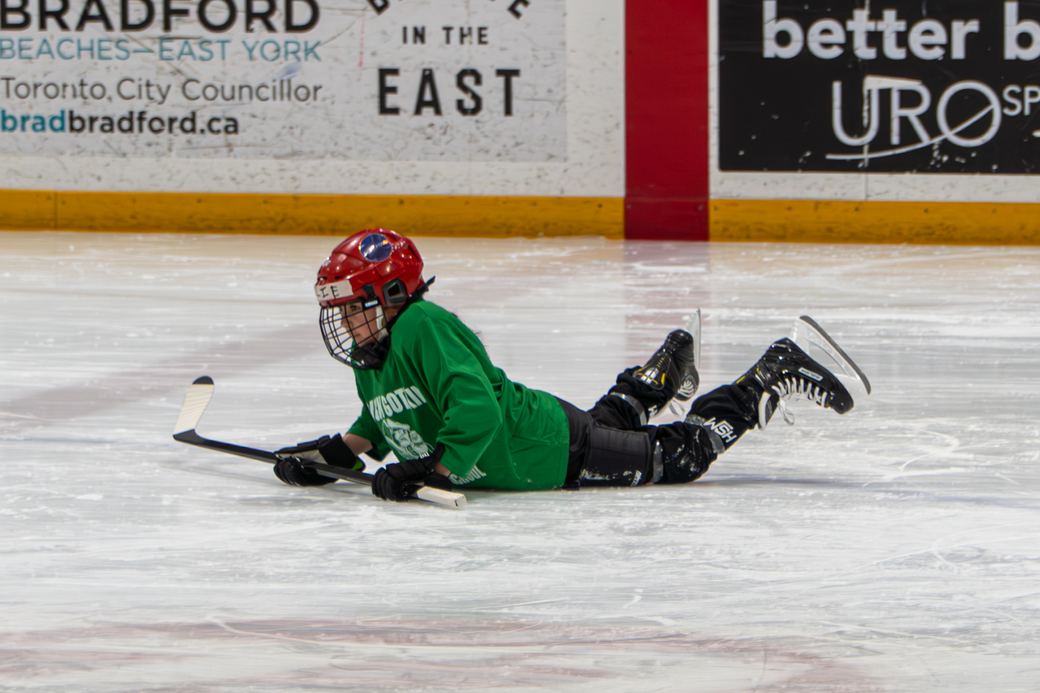 A camper who has gone down on the ice mid-drill, stick still in hand