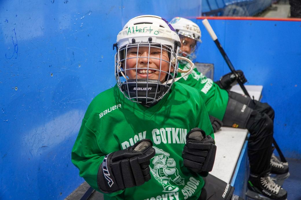 A camper in a green jersey and white helmet grinning on the ice