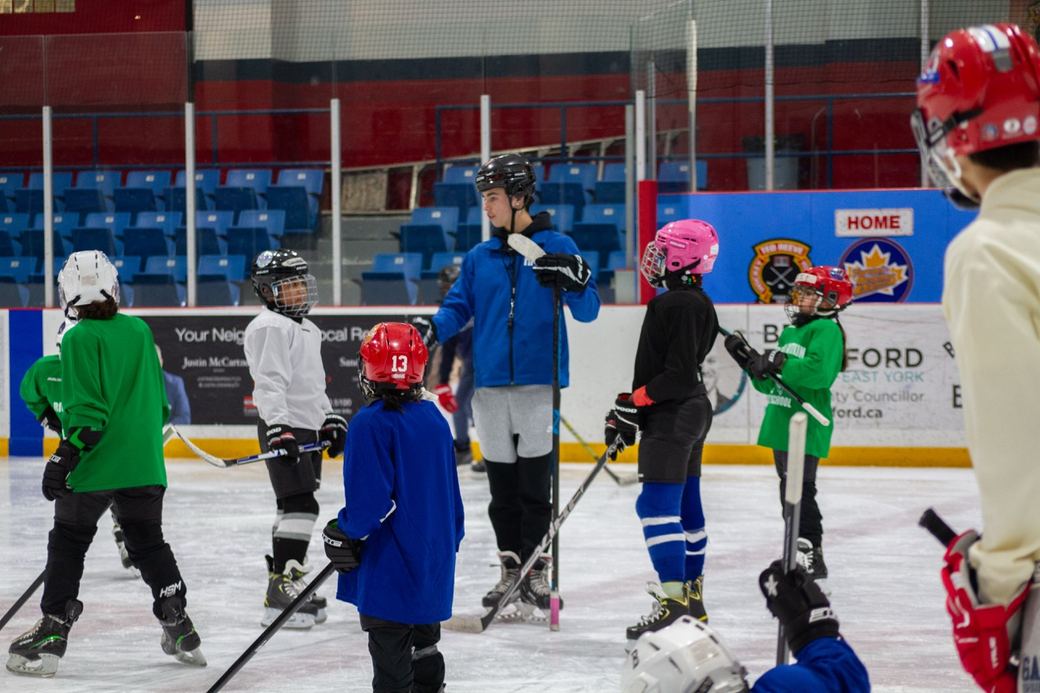 A row of campers in helmets waiting their turn at the side of the rink