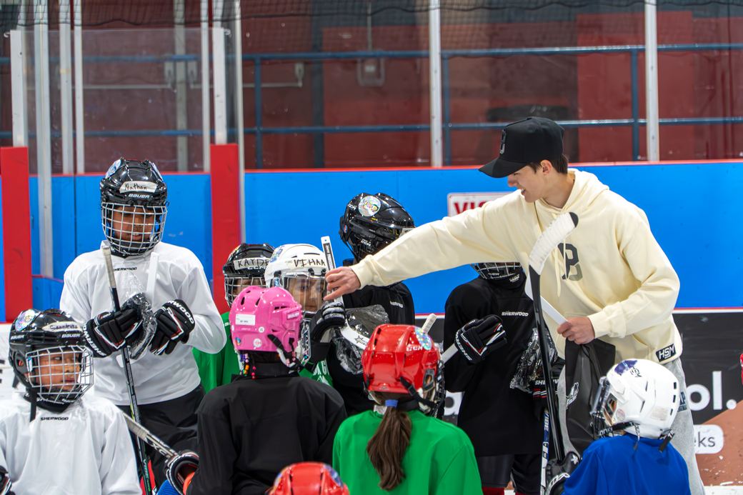 A volunteer in a cream hoodie pointing out kit to a group of campers