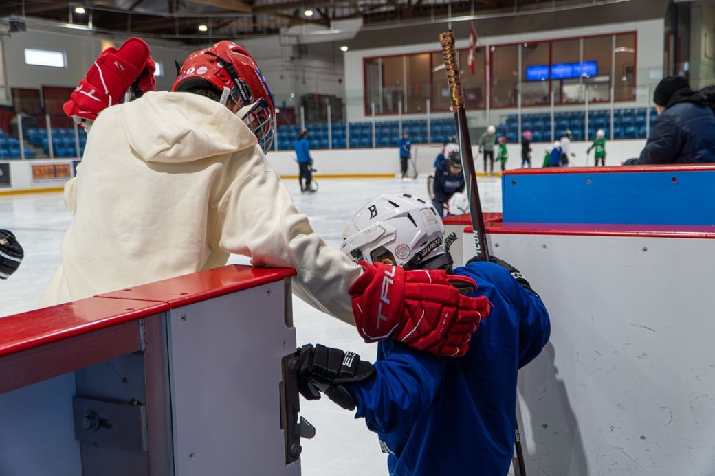 A camper being helped into their equipment at the side of the rink