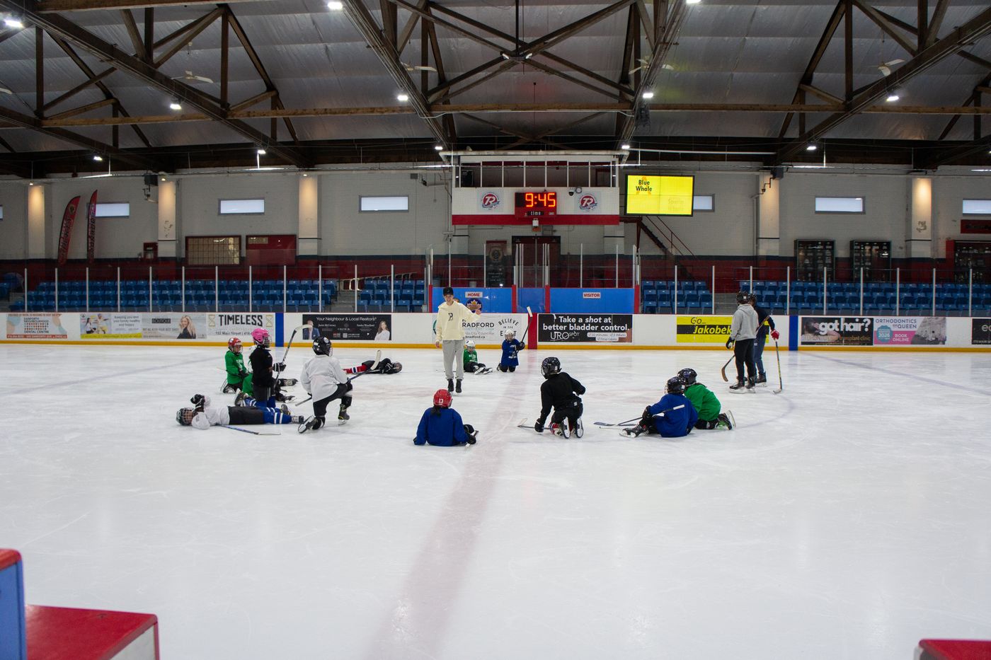 Campers seated on the ice in a wide circle around their coaches at the end of a session