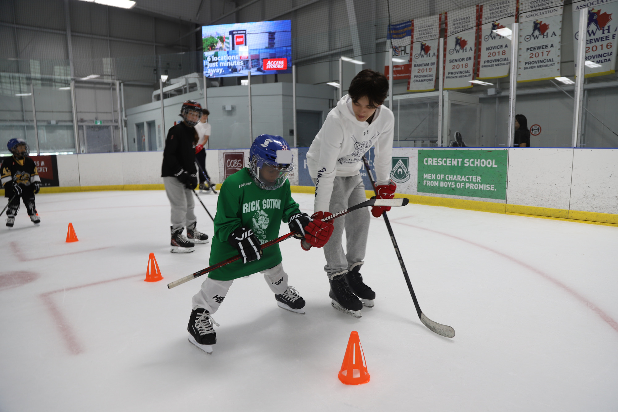 A volunteer skating alongside a young camper in a green jersey, guiding them through a line of orange pylons