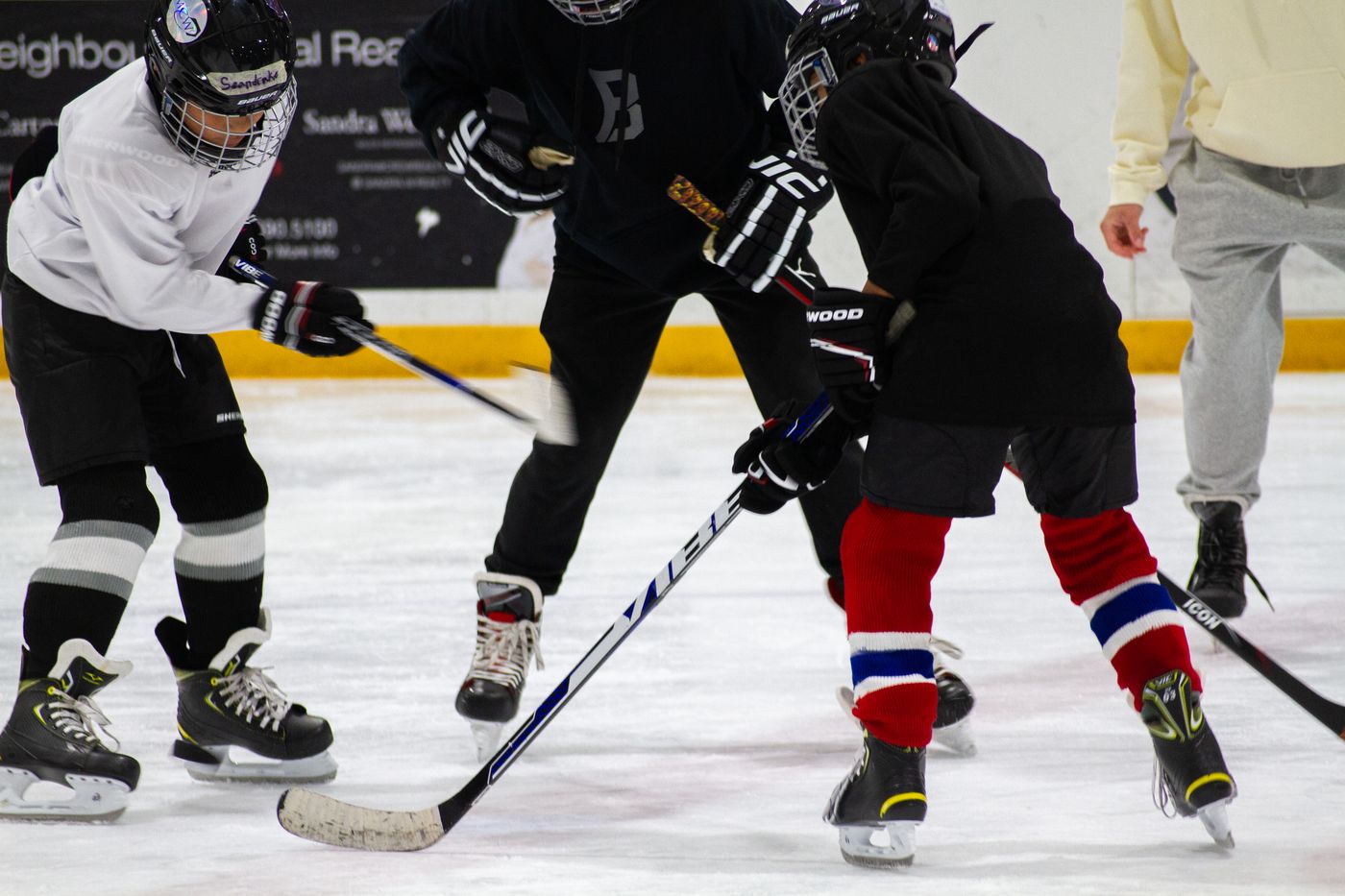 Three campers battling for a puck in a small area drill, sticks low and skates digging in